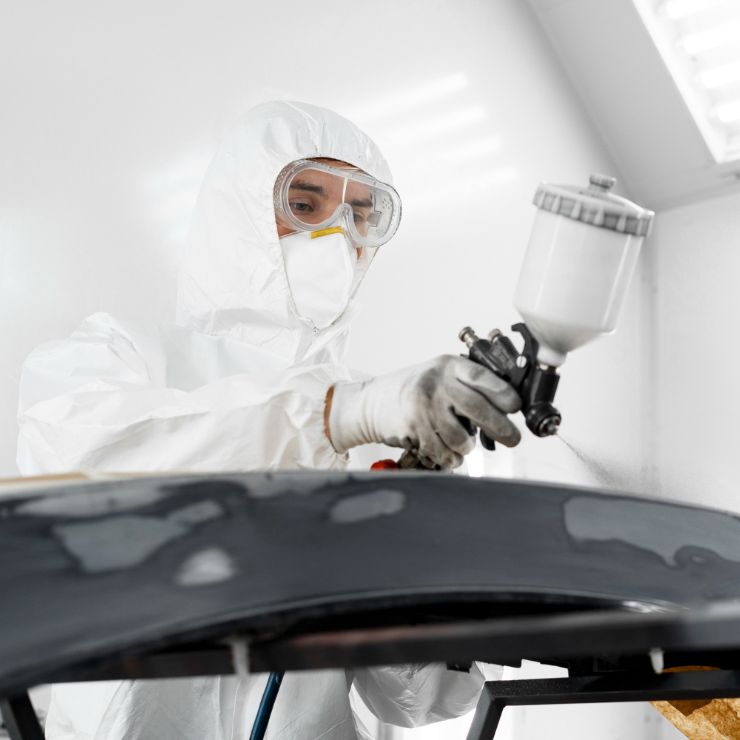 Nærbilde av en mann i verneutstyr som lakkerer en bildel